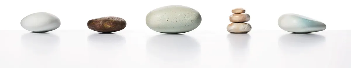 Five solidified pet remains stones in a row, showing the natural range of colors from pale grey and bronze to sage green, tan, and blue-grey.